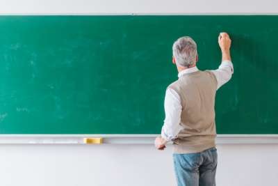 male professor writing on the blackboard with his back turned to the audience male teacher writing on the blackboard