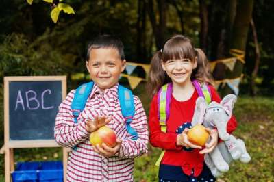 two young school students holding big apples and smiling boy and girl smiling on camera