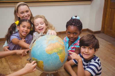 happy young students sitting around the globe