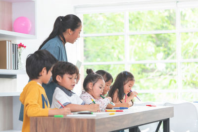 students seating at the desk, teacher supervising