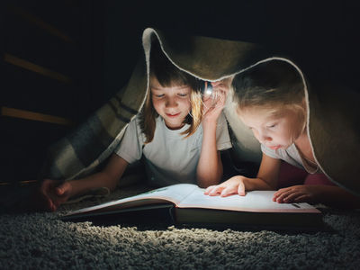 two girls under the blanket reading